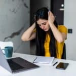 A frustrated woman works from home on her computer and holds her head